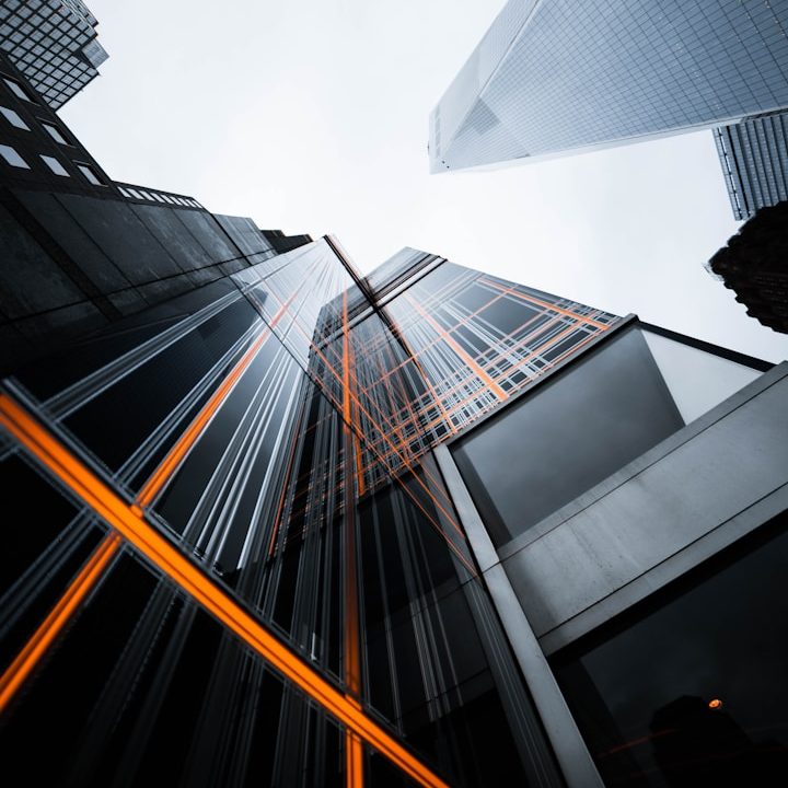 Perspectiva hacia arriba de rascacielos con detalles en naranja y cielo gris.