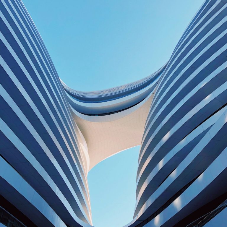 Vista de un edificio moderno con líneas curvas y franjas bluces contra un cielo claro.
