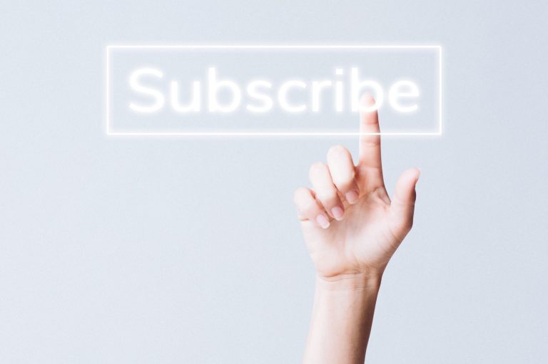Mano tocando un botón que dice "Subscribe" en un fondo claro.