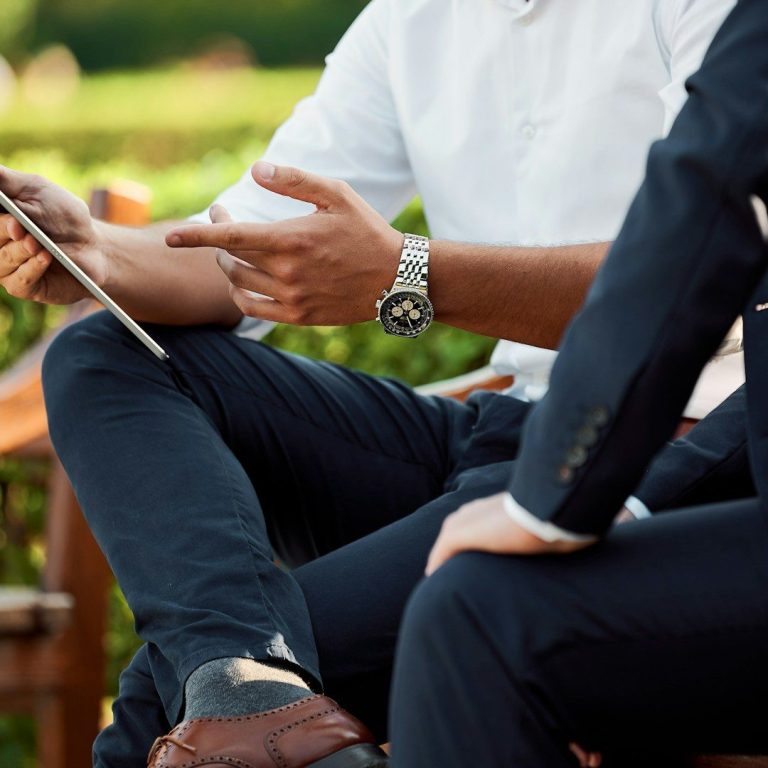 Dos hombres conversando, uno sostiene una tablet y el otro escucha atentamente.