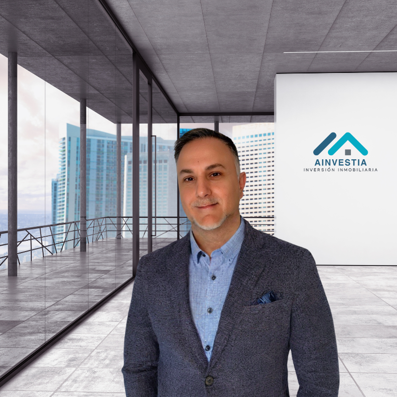 Hombre de pie en un moderno entorno de oficina con grandes ventanales y logotipo de la empresa.